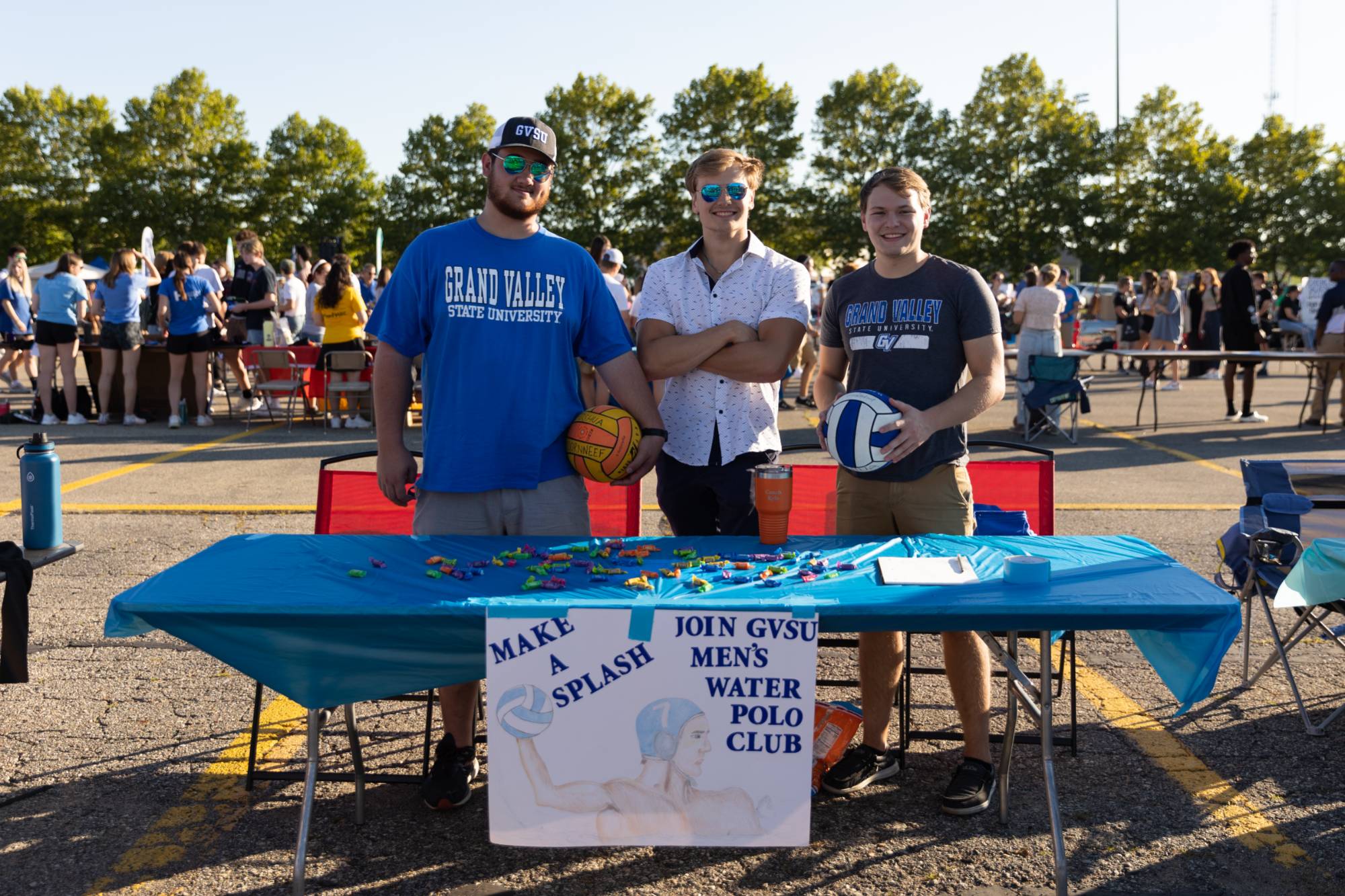 Three GVSU students post in front of a "Join GVSU Men's Water Polo Club" sign at Campus Life Night